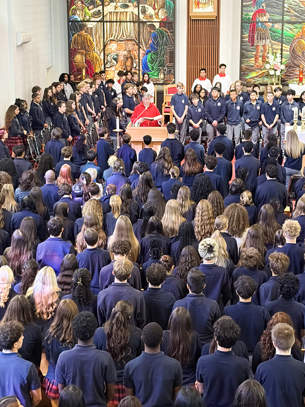 Redmond students and staff attend the Mass in the church, facing the spakers with huge sweeping religious stained glass mural artwork beyond the speakers
