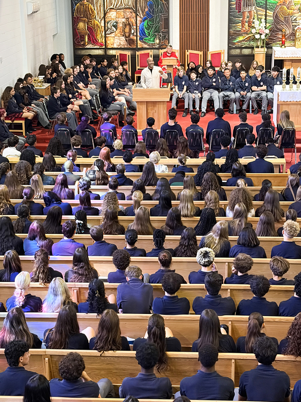 Redmond students and staff attend the Mass in the church, facing the spakers with huge sweeping religious stained glass mural artwork beyond the speakers