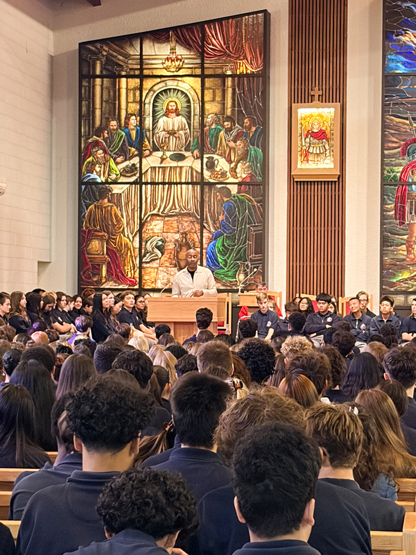 Redmond students and staff attend the Mass in the church, facing the spakers with huge sweeping religious stained glass mural artwork beyond the speakers