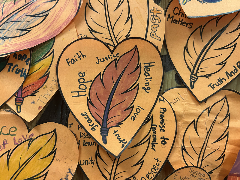 Photo of a few of the orange hearts showing the messages the students have written on them, with each heart having a drawing of a feather in the middle of it