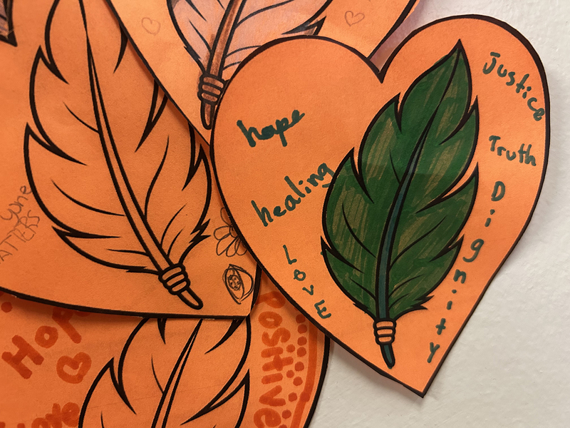 Photo of a few of the orange hearts showing the messages the students have written on them, with each heart having a drawing of a feather in the middle of it