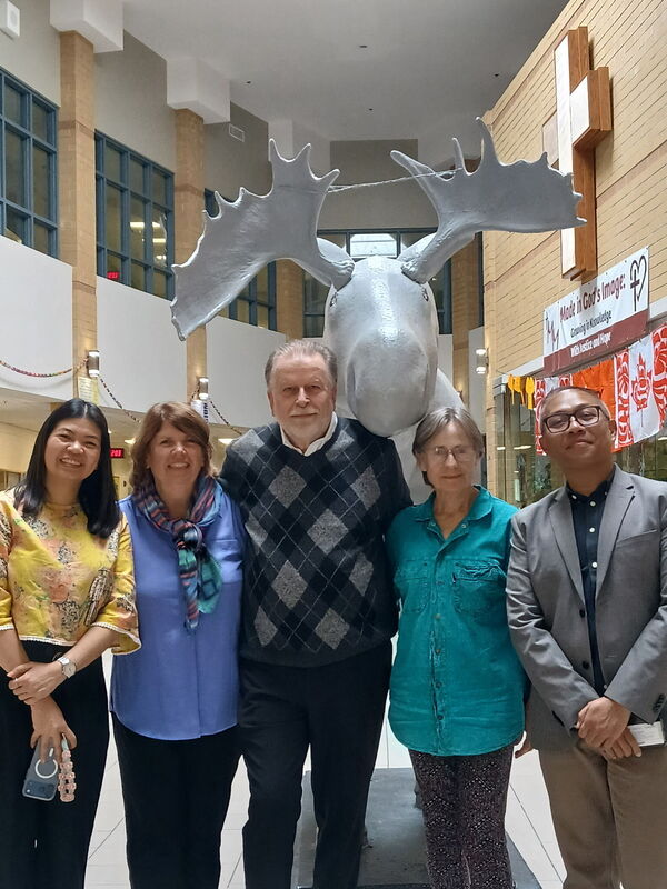 5 adults posing in a school in front of a giant moose sculpture