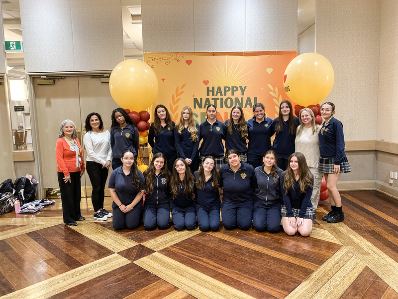 Group photo of Loretto College students posing with staff at Villa Colombo in front of a banner that says Happy National Seniors Day