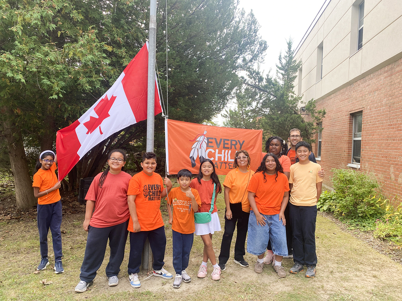 St. Malachy students and staff in orange shirts pose beside a Canadian flag and an “Every Child Matters” banner outside the school in honour of the National Day for Truth and Reconciliation