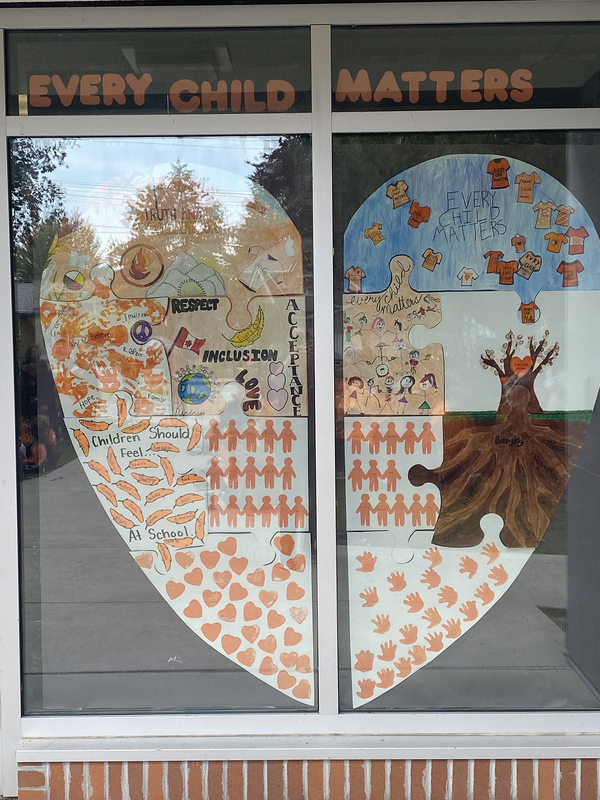 Photo of the window display of the large heart assembled from the puzzle pieces crafted by the students, with a banner above it that reads "Every Child Matters" in orange on a black background