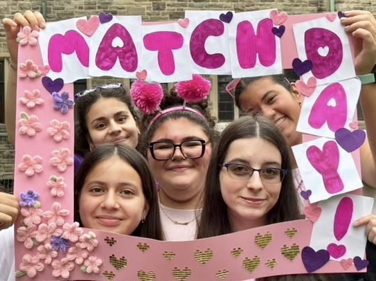 Students pose through a crafted pink frame that says Match Day!