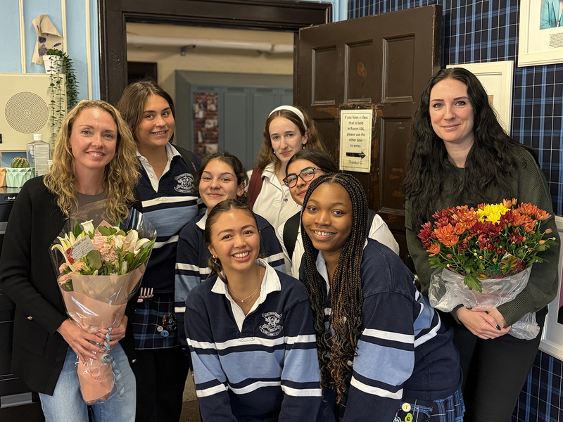 Group photo of Loretto Abbey students in their uniforms, posing with two teachers holding flowers