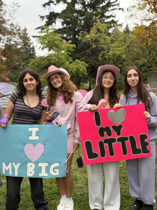 Photo of four students dressed up in casual clothing, holding two signs that says I heart my big and I heart my little