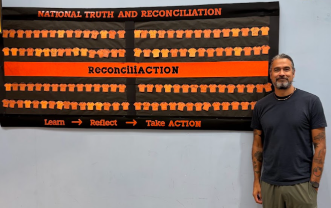 A man stands to the right of a wall display reading “NATIONAL TRUTH AND RECONCILIATION” and “ReconciliACTION,” with repeating orange-and-black blocks and the steps “Learn → Reflect → Take Action.”