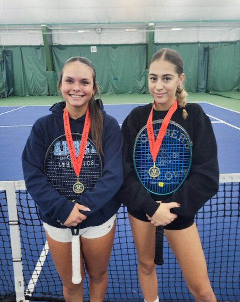 Photo of Juliana and Sophia on the court with their tennis rackets wearing their championship medals