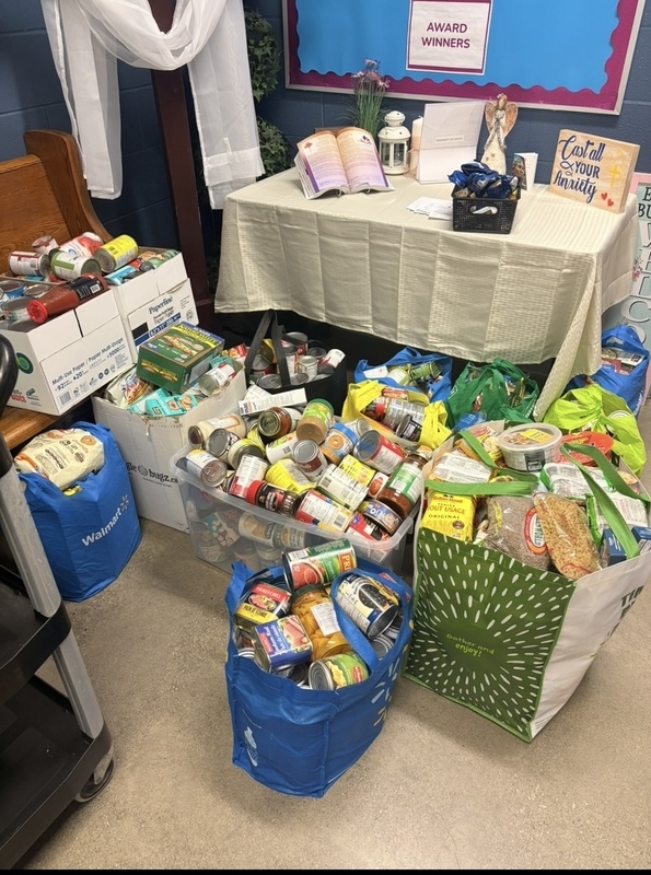 Bins and bags of assorted packaged food items and pantry staples arranged on the floor beside a bench in a room with blue walls.