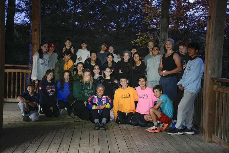 Group photo of Redmond students and staff posing together in their lodge at Camp Muskoka in twilight, with the trees behind them