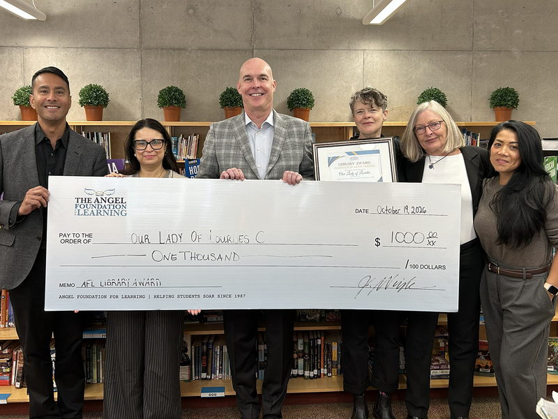 Andrea, in addition Our Lady of Lourdes Catholic School and Angel Foundation for Learning staff pose together with an oversized $1,000 Angel Foundation donation check in an office