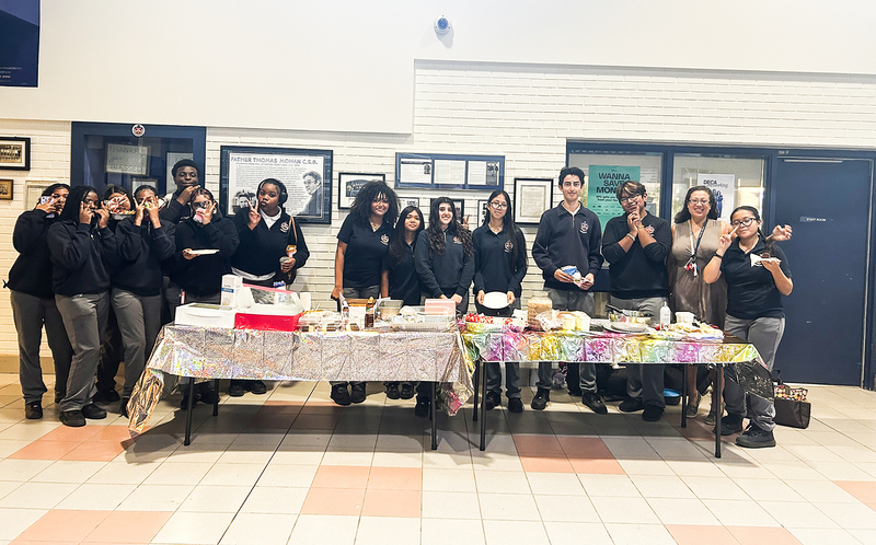 Photo of Father Henry Carr students posing together behind two tables holding food of Latin and Hispanic cultures for the students to appreciate