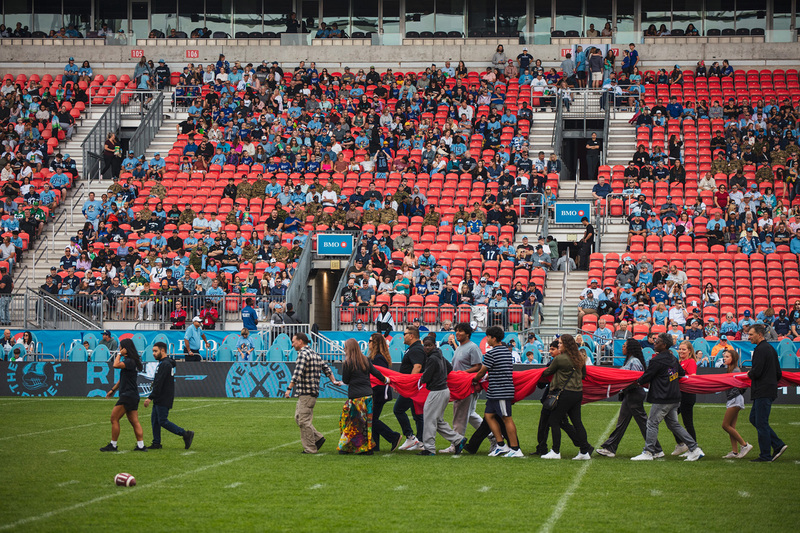 Photo of Coach Vescio and students on the field carrying along a huge Canada flag