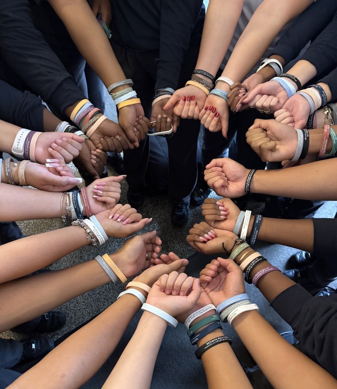 A group of students standing in a circle showing their wrists, each wearing a blessed bracelet from the school Mass.