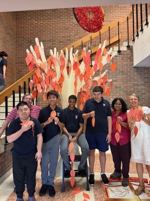 Group photo of SJHN students and staff in front of the tree holding their leaves