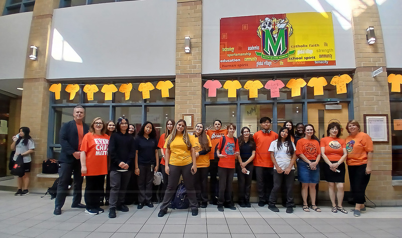 Group photo of Marshall McLuhan students and staff in front of a display of cardboard orange shirts