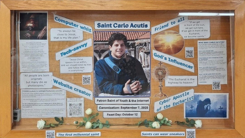 Display board about the life of Saint Carlo Acutis, with a picture of Carlo in the middle, surrounded by informational tidbits about his life