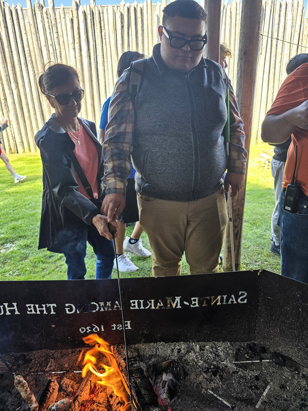 Photo of Chaminade student stoking fire while being helped by a teacher