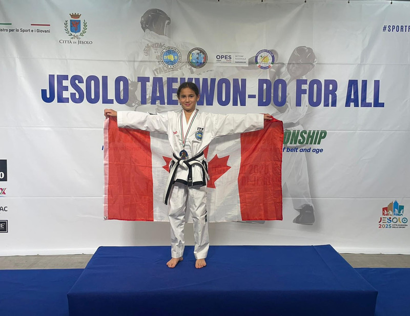 Photo of Leianna on the podium with her medal holding out the Canada flag behind her