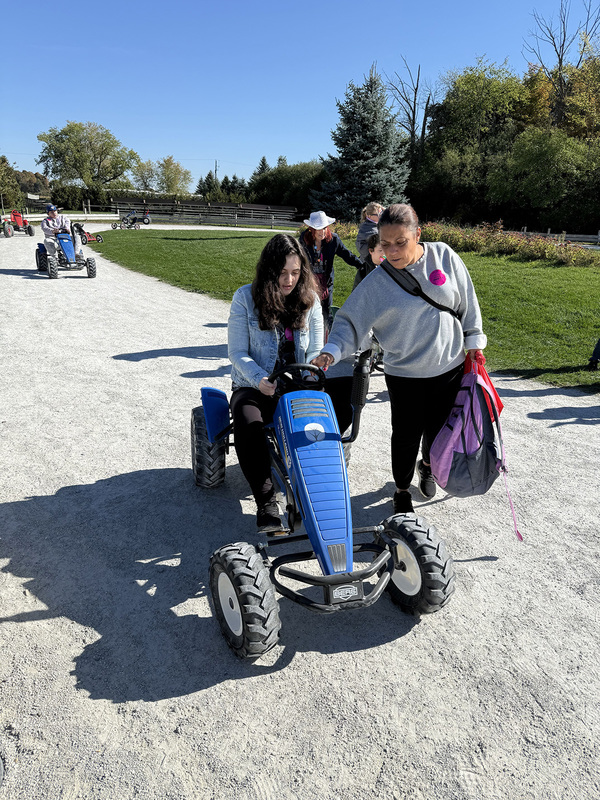 Photo of a student driving a toy truck while being helped by a teacher