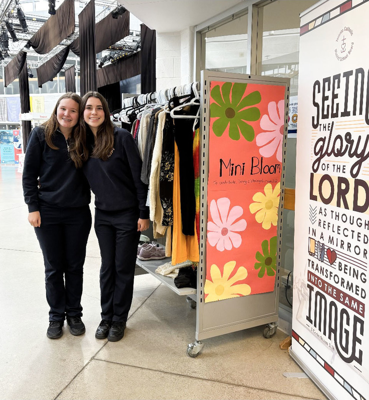 Photo of two Loretto College School students standing next to the Mini Bloom Clothing Rack full of donated clothing items