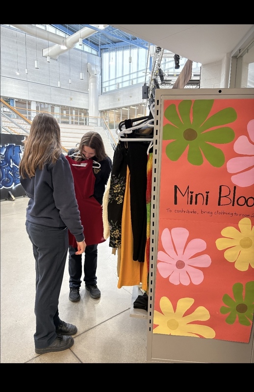 Photo of two Loretto College School students sizing up clothing from the Mini Bloom Clothing Rack full of donated clothing items