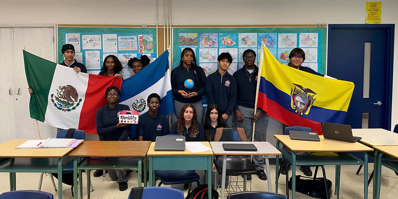 Group photo of Father Henry Carr students waving country flags as ewll as holding up a globe and a box of Timbits