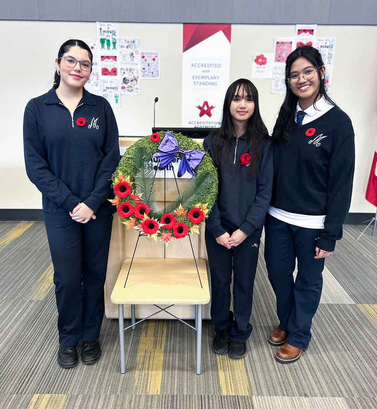 Group photo of the three Madonna students performing at the event, posing with the wreath