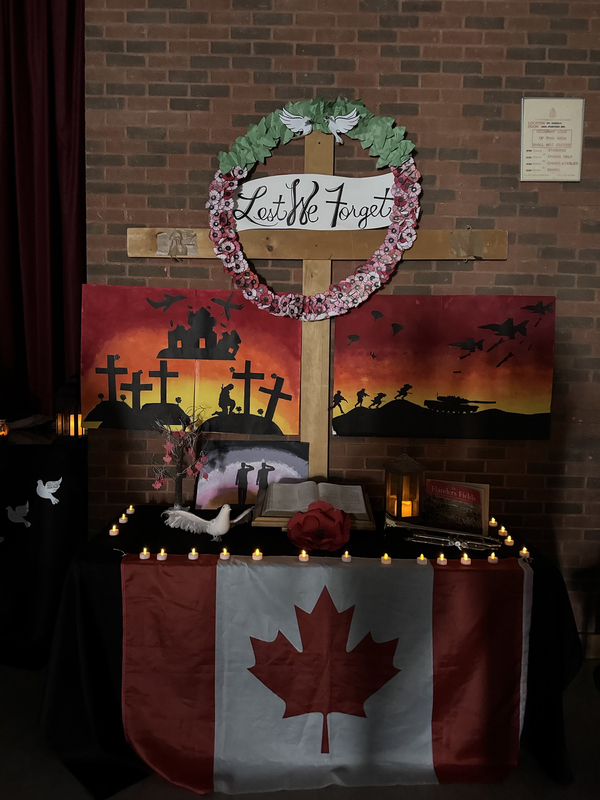 "Lest We Forget" display for Remembrance Day featuring a wreath, poppies, white peace doves, Canada flag, artwork of soldiers, the Bible and candles