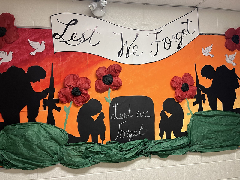 Photo of display for Remembrance Day featuring poppies, silhouettes of soldiers and graves, and the words "Lest We Forget"