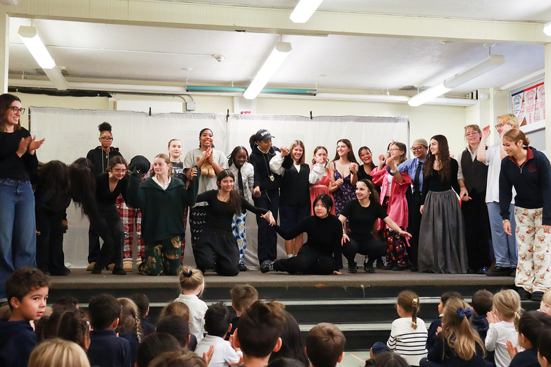 Group photo of Notre Dame theatre players bowing on stage while St. John students watch and clap from the audience
