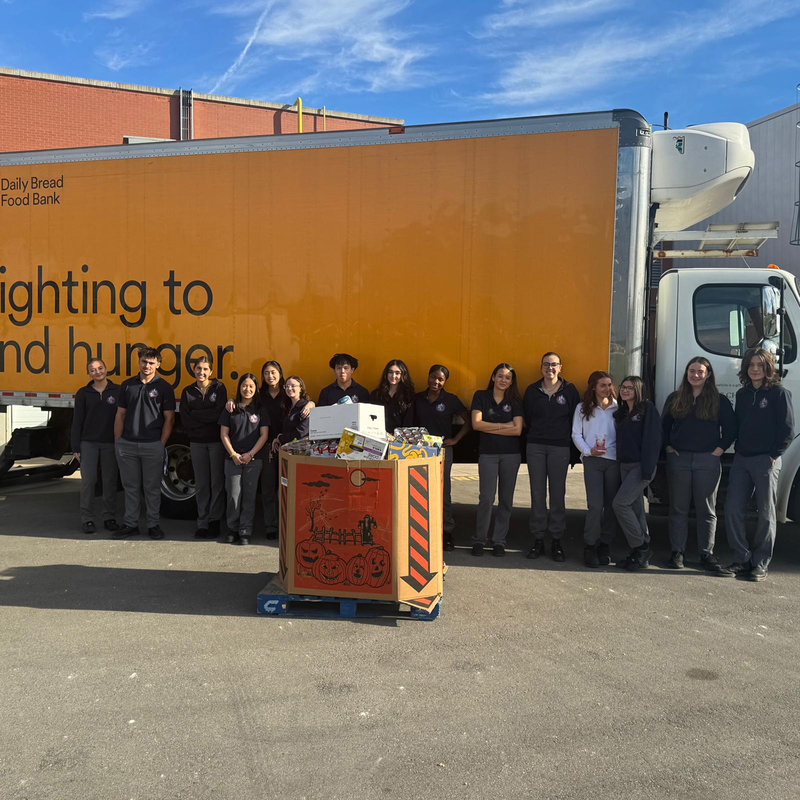 Group photo of Redmond students standing in front of the Daily Bread Foodbank pickup truck, with a large box of the food items collected in front of them
