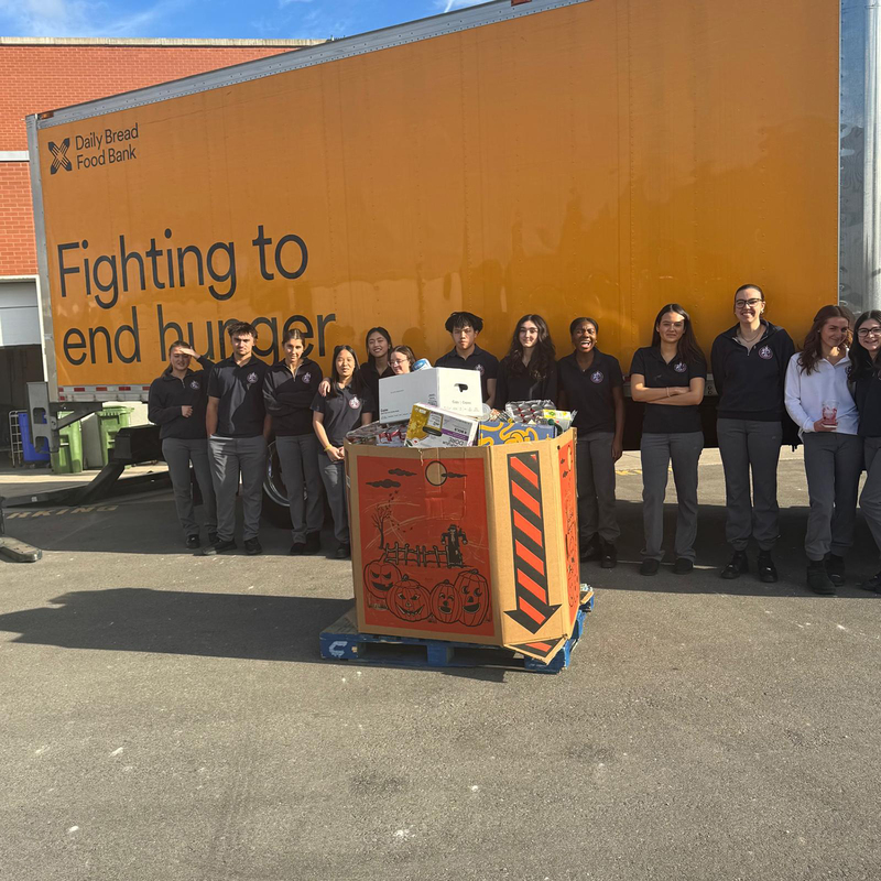 Group photo of Redmond students standing in front of the Daily Bread Foodbank pickup truck, with a large box of the food items collected in front of them