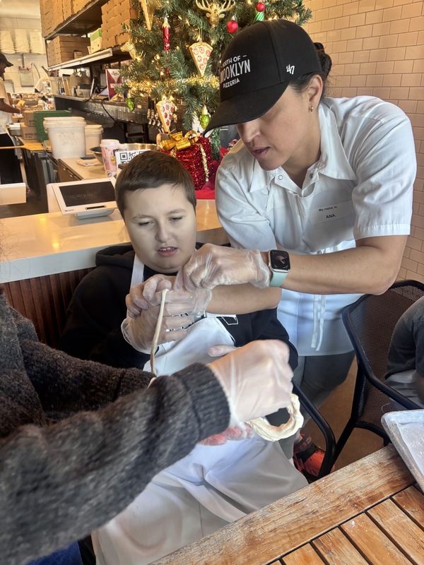 Photo of pizza worker showing student how to roll dough