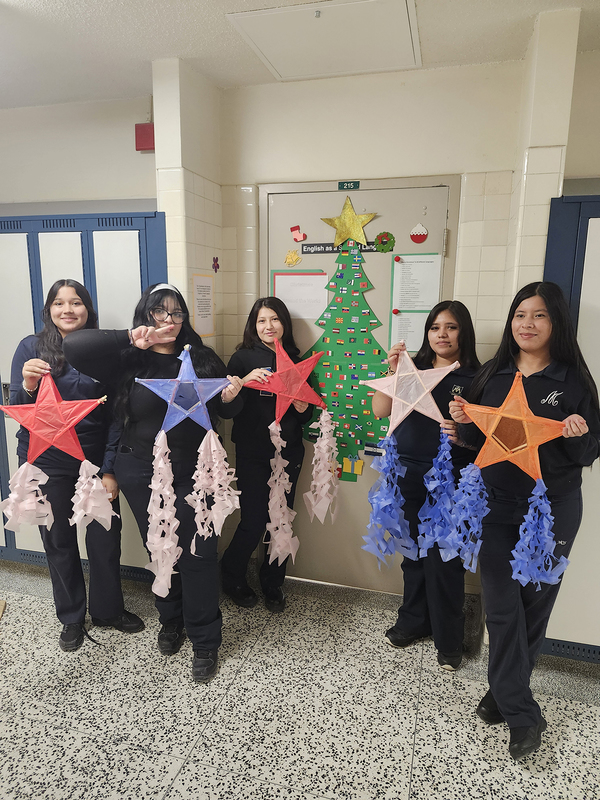 Photo of students holding up the Parols they made in front of a Christmas tree display