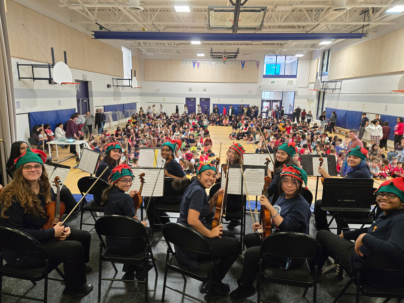 Photo of MPJ Strings students with their instruments and Christmas hats, ready to perform to the elementary students