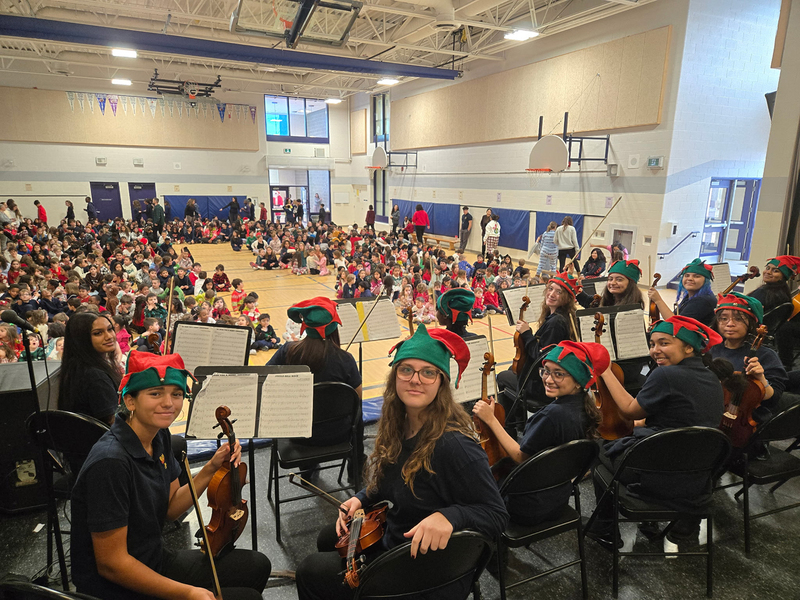 Photo of MPJ Strings students with their instruments and Christmas hats, ready to perform to the elementary students