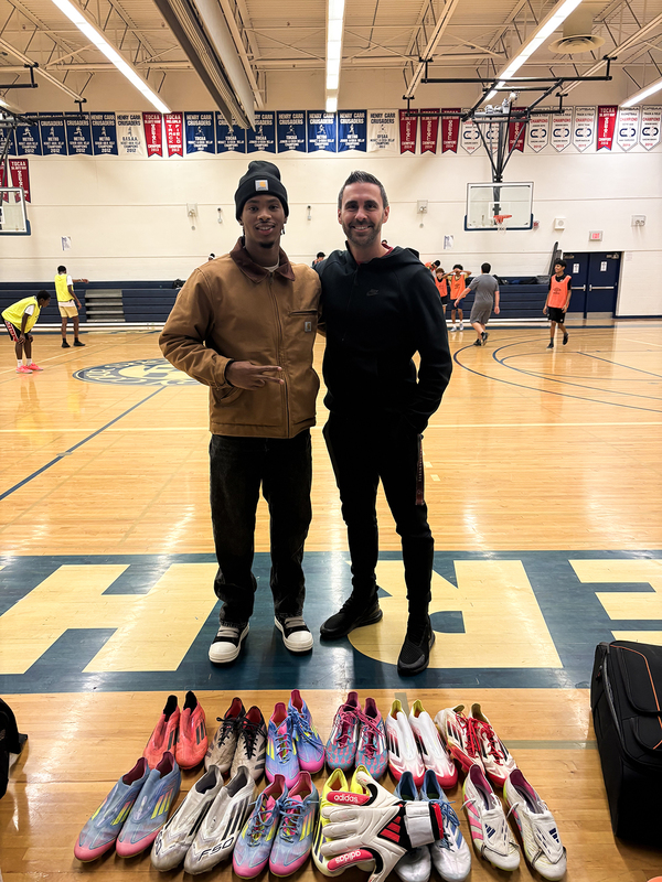 Photo of Kimani with coach in the Father Henry Carr gymnasium with the donated shoes laid out in front