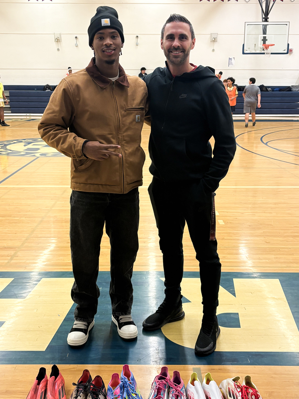 Photo of Kimani with coach in the Father Henry Carr gymnasium with the donated shoes laid out in front