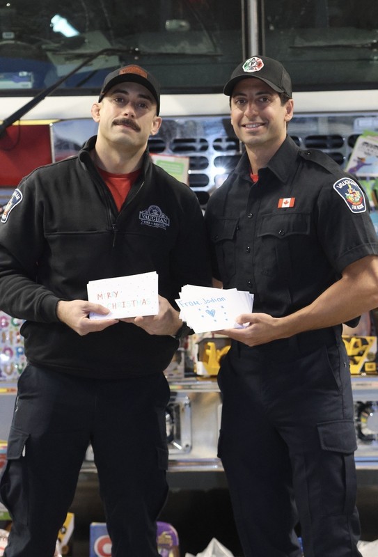 Photo of two firefighters holding up the holiday cards designed by Madonna students