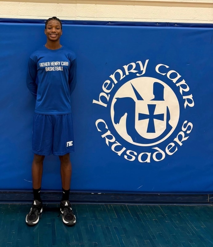 Photo of Smith in basketball uniform in from of a board that has the Henry Carr Crusaders logo on it