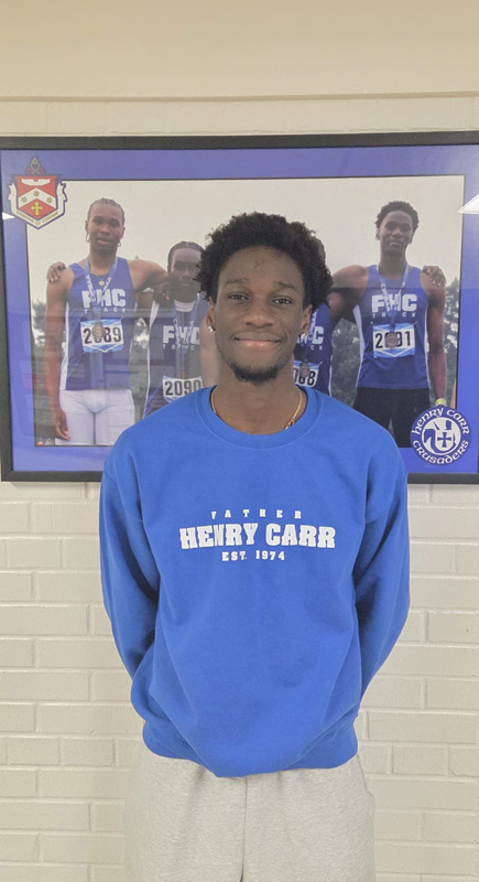 Photo of Adnan standing in a FHC sweater in front of a framed photo that shows his medalling performance