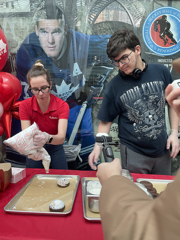 Photo of Tim Hortons staff member helping a student to make donuts