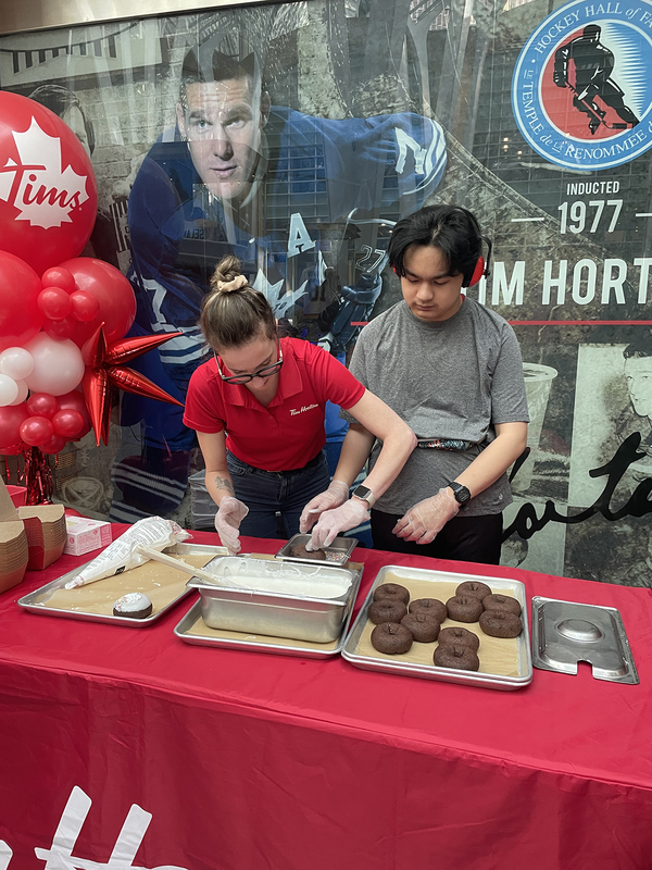 Photo of Tim Hortons staff member helping a student to make donuts