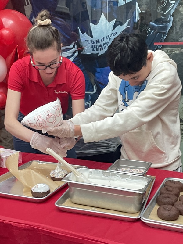 Photo of Tim Hortons staff member helping a student to make donuts