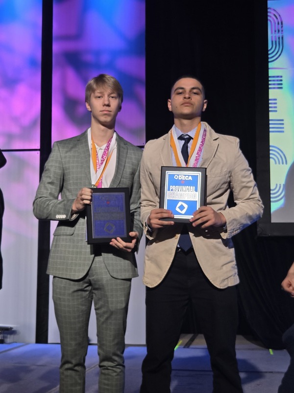 2 students posing dressed up in business attire, and with medals around their necks. 
