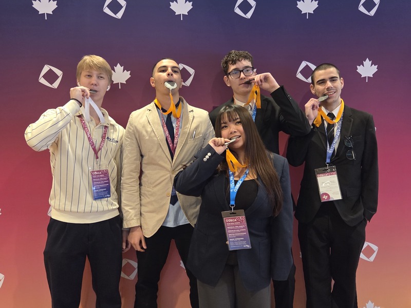 7 students posing dressed up in business attire, and with medals around their necks. 