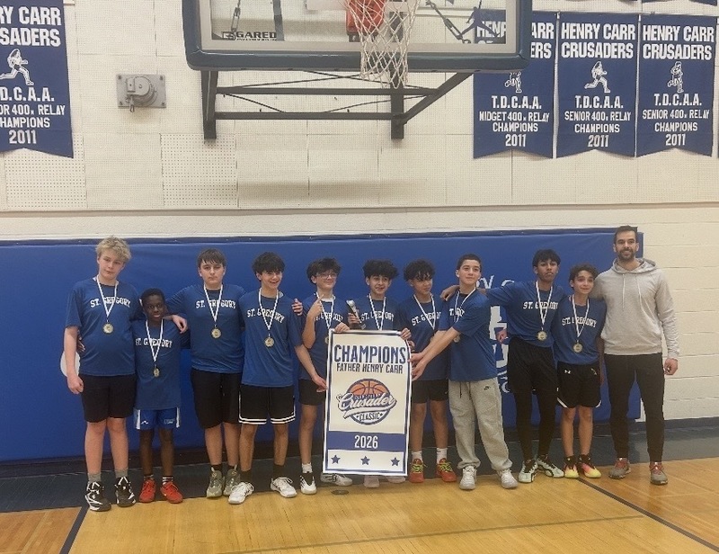 A boys basketball team photo in the gym, holding up a Champions 2026 banner